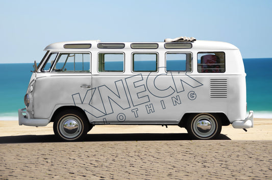 A white VW Camper van parked on a beach with the blue sea and blue sky in the background. The Camper has "KNECK Clothing" embossed diagonally on the side.